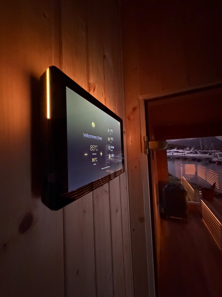 The Ulmatic guest screen mounted in a sauna, showing temperature and a marina view